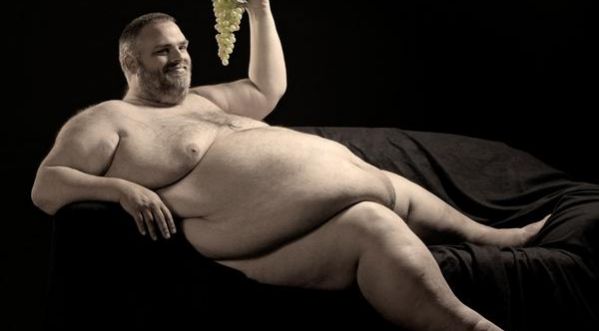 homme obèse gros nu sur canapé noir avec une grappe de raisin blanc